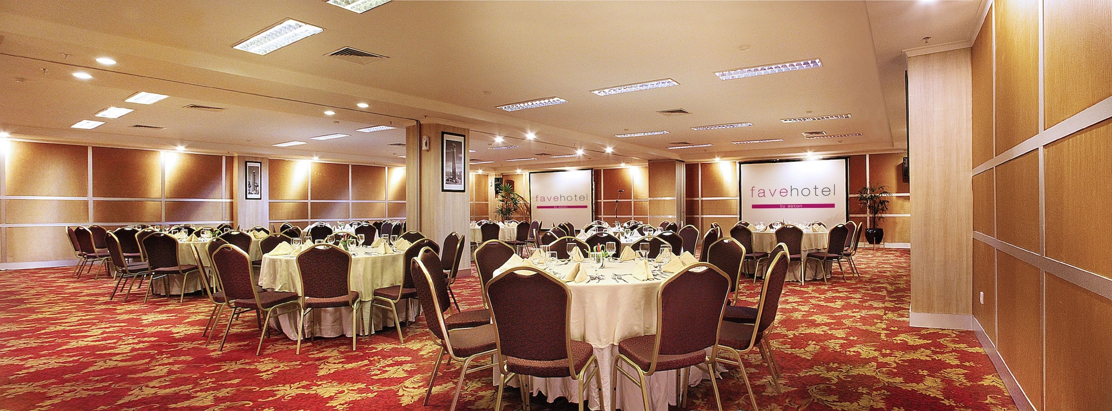 Una sala conferenze con tavoli e sedie rotonde, una moquette rossa e un cartello con la scritta 'favehotel by aston'.