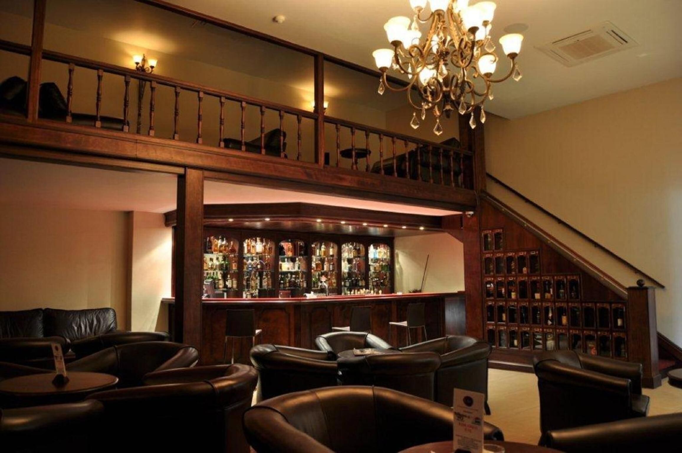 A bar area with leather seating, a staircase, and a chandelier.