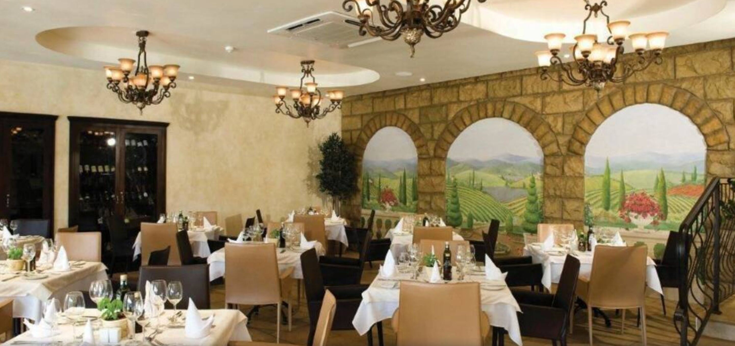 A restaurant with tables set for dining, chandeliers, and a mural of a landscape.