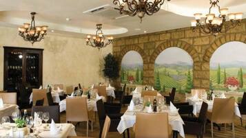 A restaurant with tables set for dining, chandeliers, and a mural of a landscape.