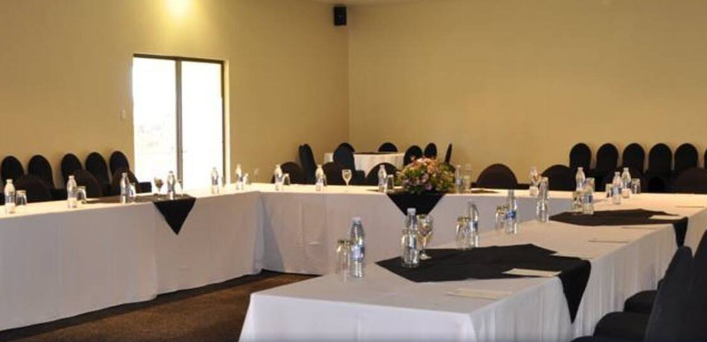 Un salón de conferencias con mesas largas, sillas y botellas de agua.