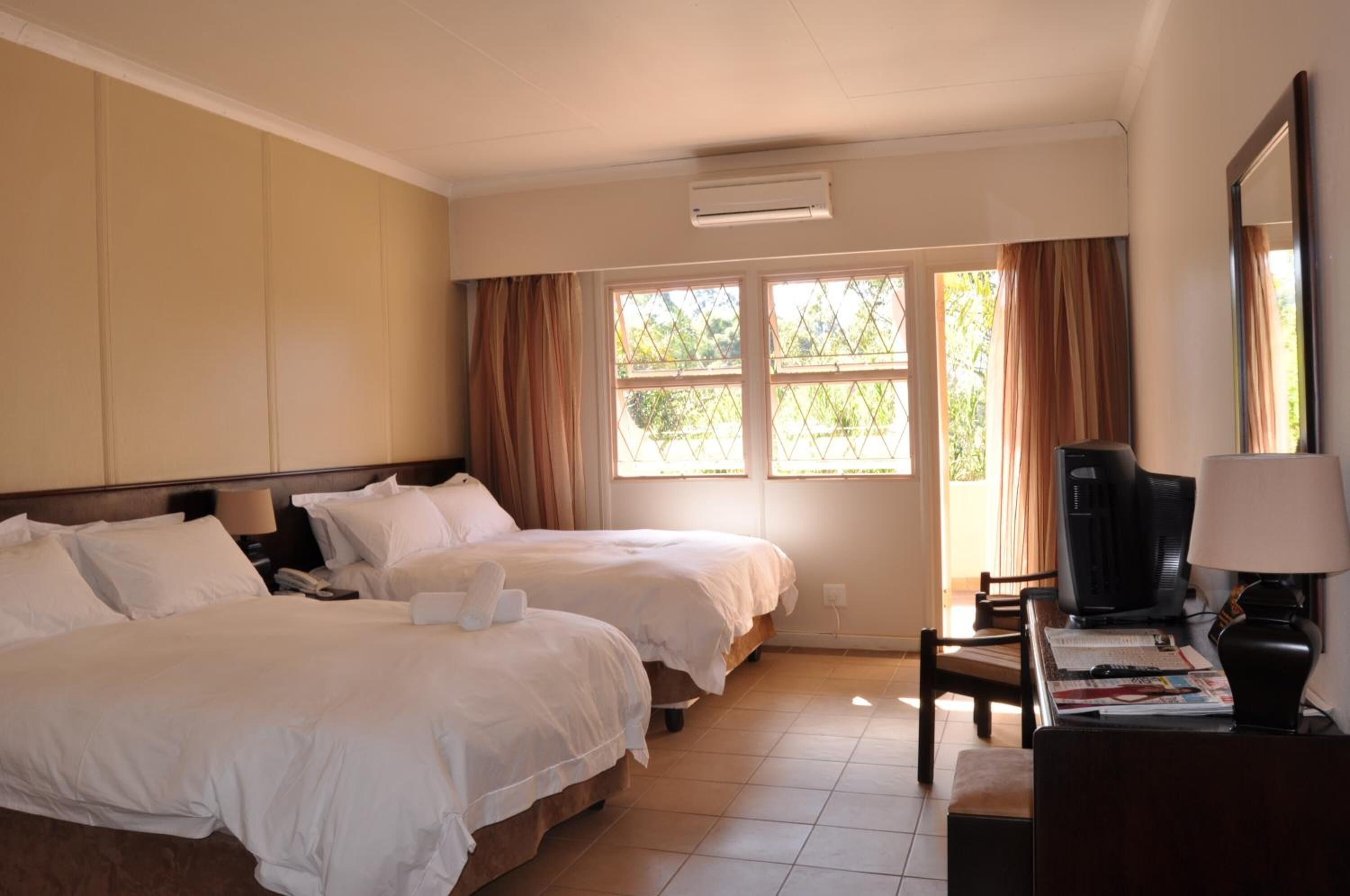 A hotel room with two beds, a desk with a chair, a television, and a window with curtains.