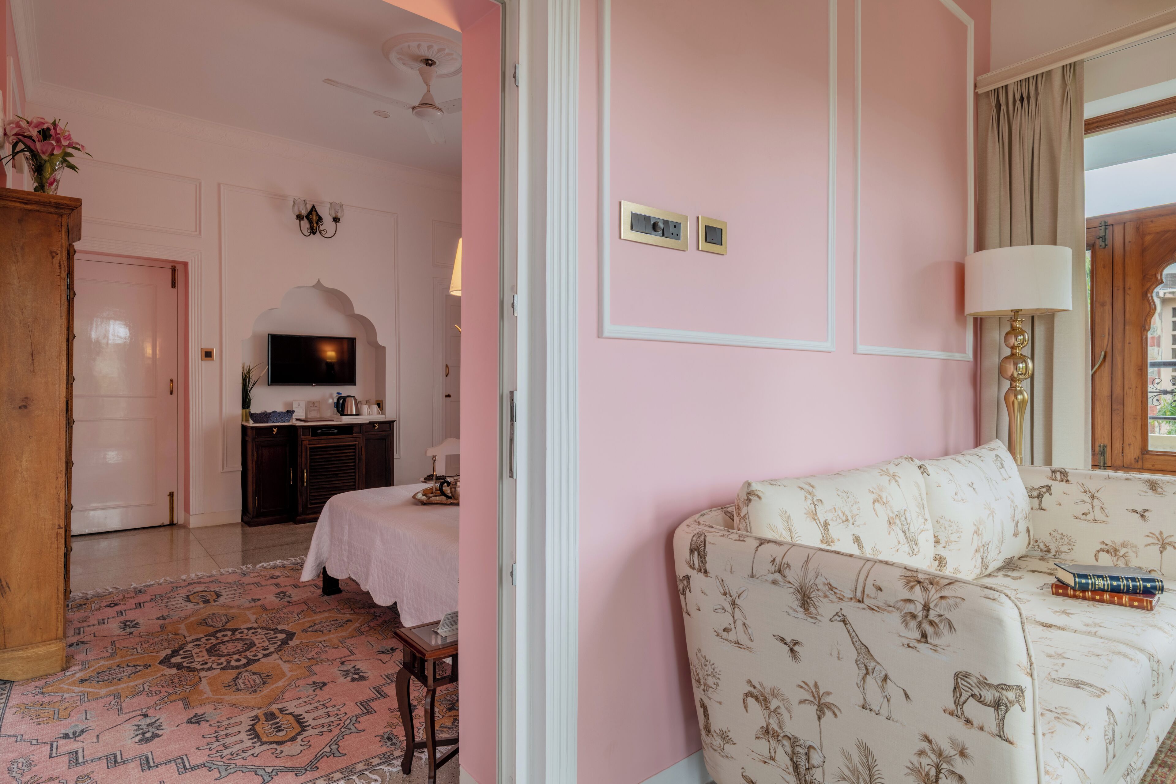 Una habitación con una pared rosa, un sofá blanco con estampado floral, un mueble de madera, un televisor y una alfombra estampada.