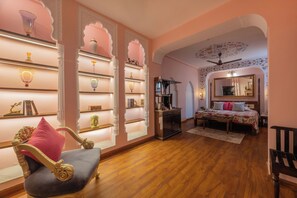 Una habitación con cama, una silla, una mesita de centro y estanterías con objetos decorativos.
