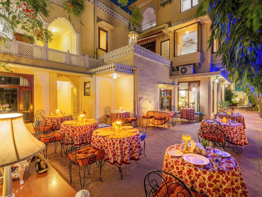 An outdoor dining area with multiple round tables, each set with plates, glasses, and cutlery.