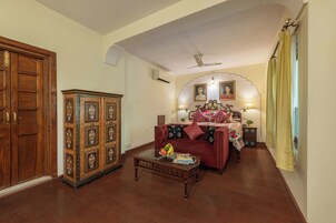 Quarto tradicional com guarda-roupa de madeira, aparador decorativo, sofá, cama com roupa de cama floral e ventoinha no teto.