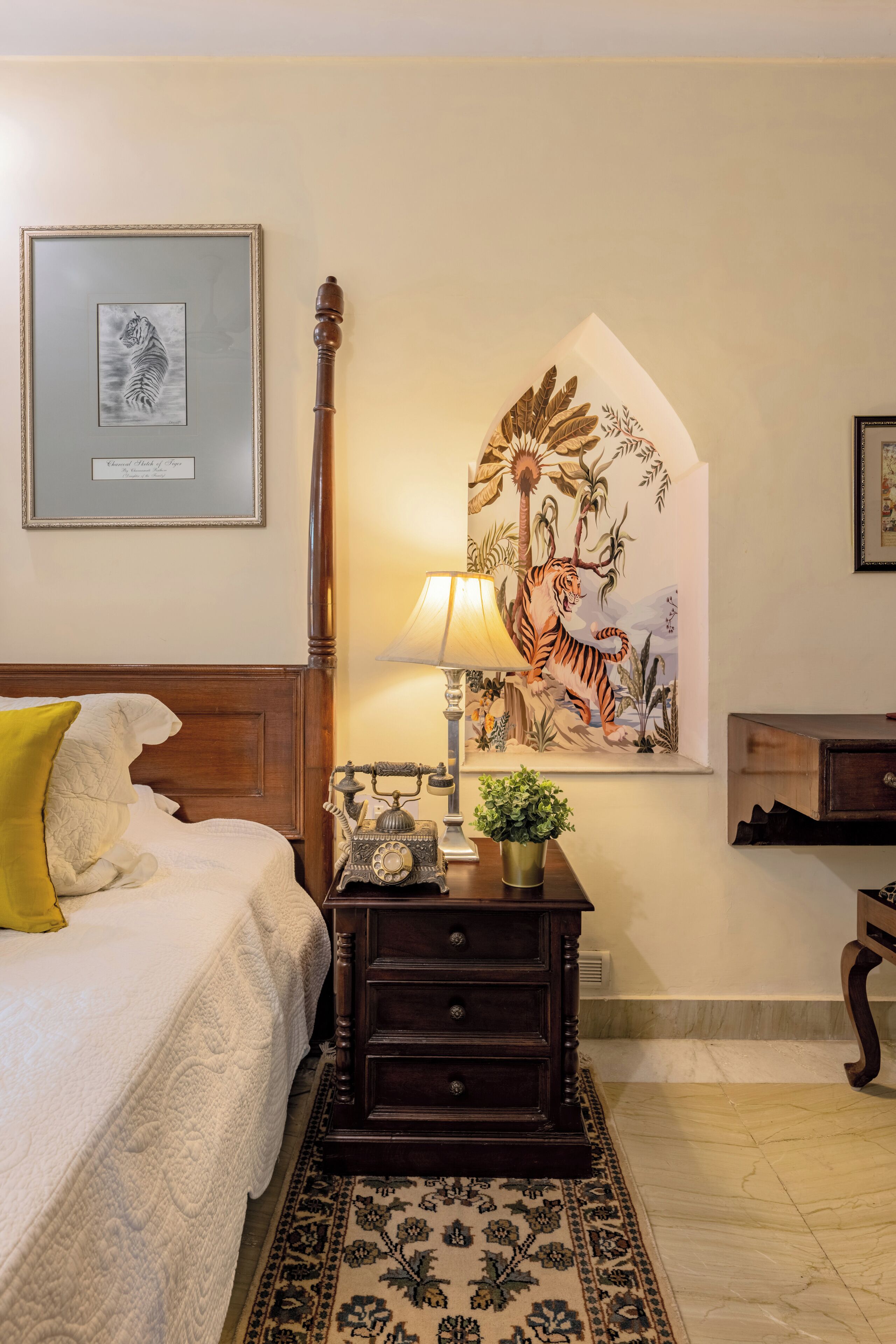 A bedroom with a bed, a nightstand, a lamp, a framed tiger picture, and a wall mural.