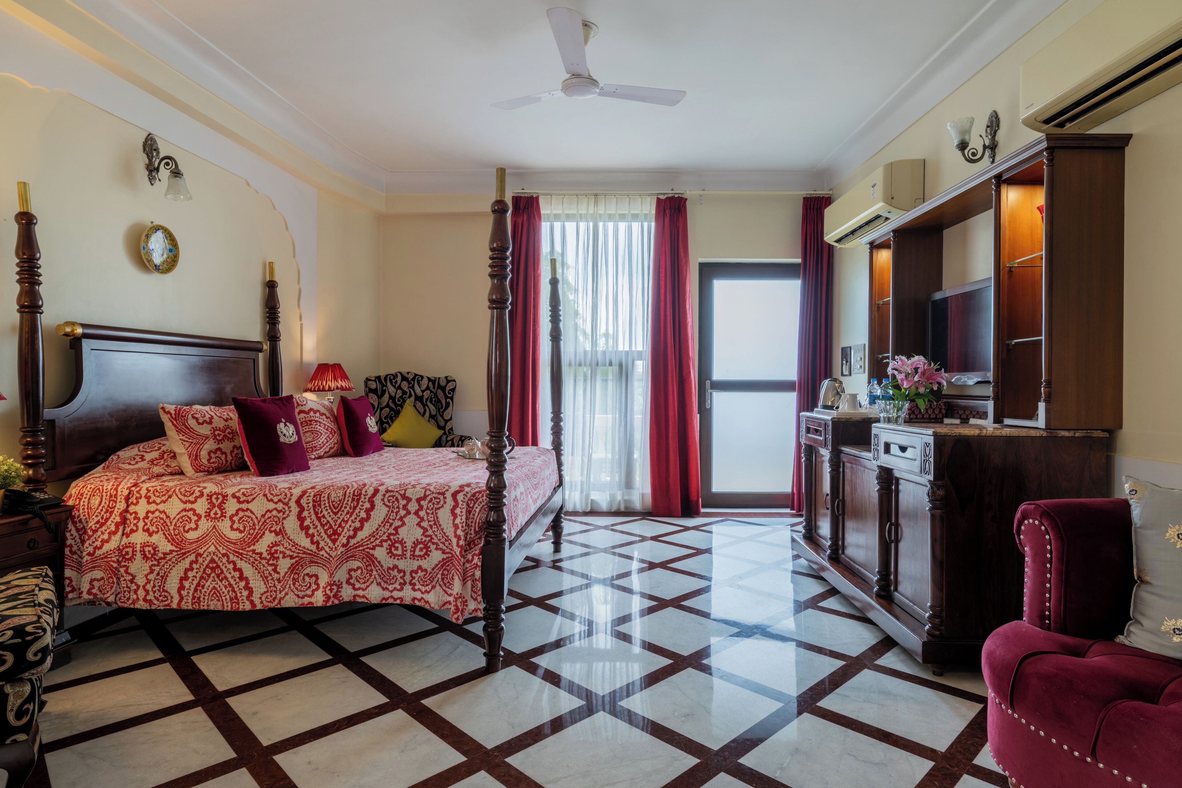 A bedroom with a four-poster bed, a desk with a mirror, and a red armchair.