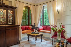 Una habitación con un armario de madera, una mesa de centro de vidrio, un sofá rojo, una mesa de vidrio con un florero y una ventana con cortinas.