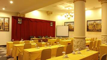 A conference room with tables set for a meeting, a red curtain backdrop, and classical architectural details.