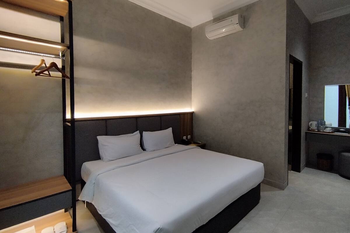 Ein modernes Hotelzimmer mit einem großen Bett, einem Nachttisch, einem integrierten Kleiderschrank und einer kleinen Sitzecke mit Tisch und Stühlen.