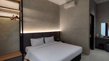 A modern hotel room with a large bed, a bedside table, a built-in wardrobe, and a small seating area with a table and chairs.