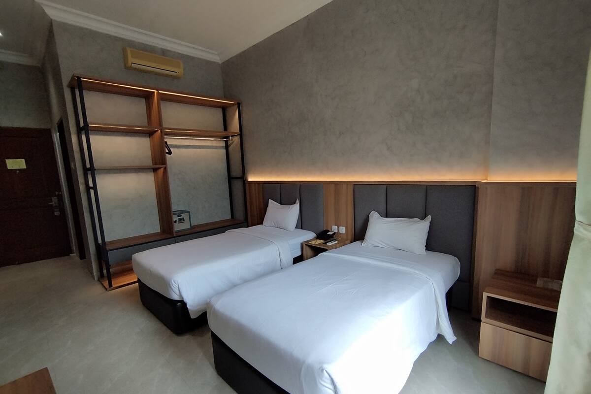 Ein Hotelzimmer mit zwei Betten, einem großen Spiegel, einem Nachttisch mit Telefon und einem Holzregal.