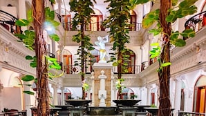 A courtyard with a central fountain, surrounded by tables and chairs, and two large trees with vines. - The Grand Palace Hotel Malang (Malang)