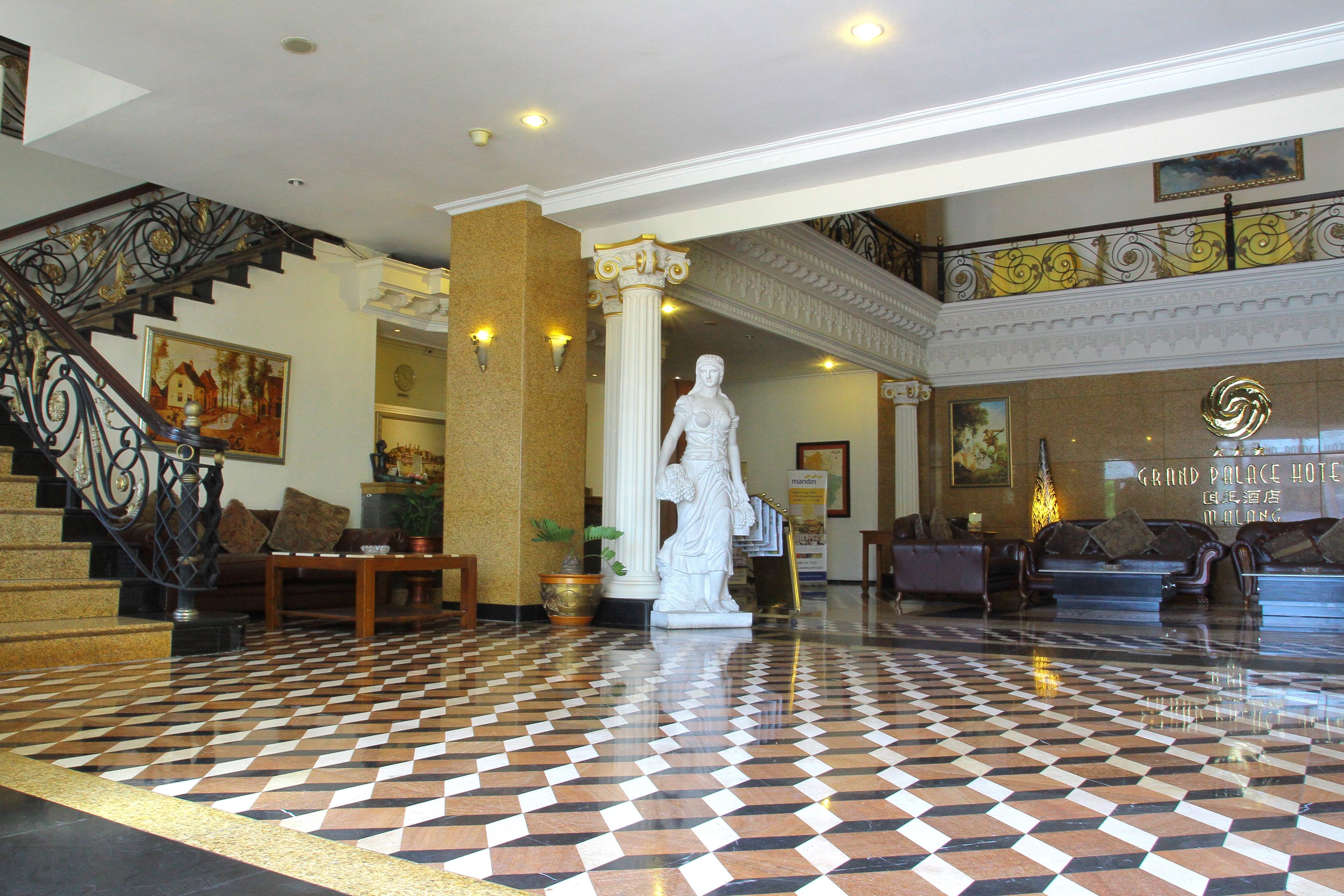 A lobby with a checkered floor, a statue, a staircase with ornate railings, and a Grand Palace Hotel sign.