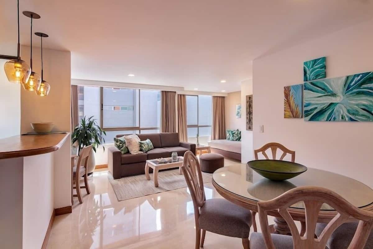 Un salon moderne avec un canapé, une table basse et une table à manger. De grandes fenêtres offrent une vue sur l’extérieur.