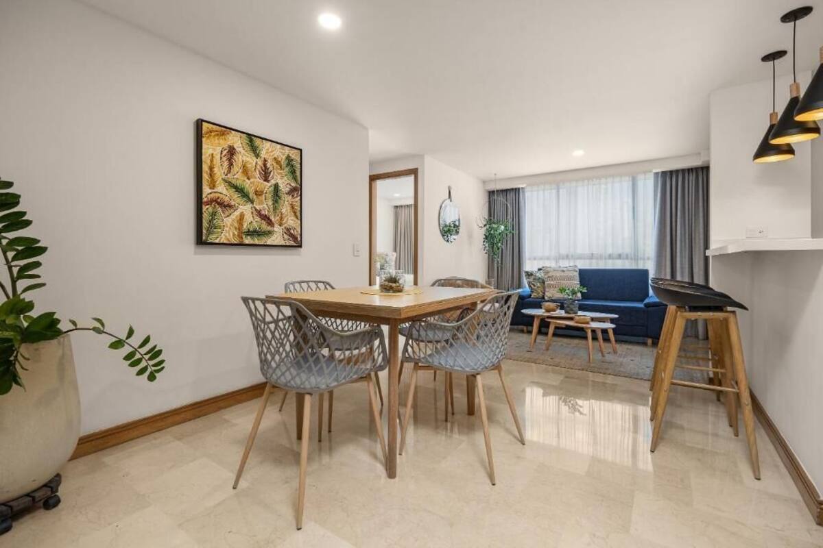 Un salon moderne avec un coin repas, comprenant une table à manger en bois, des chaises grises en osier, un canapé bleu et un grand tableau accroché au mur.