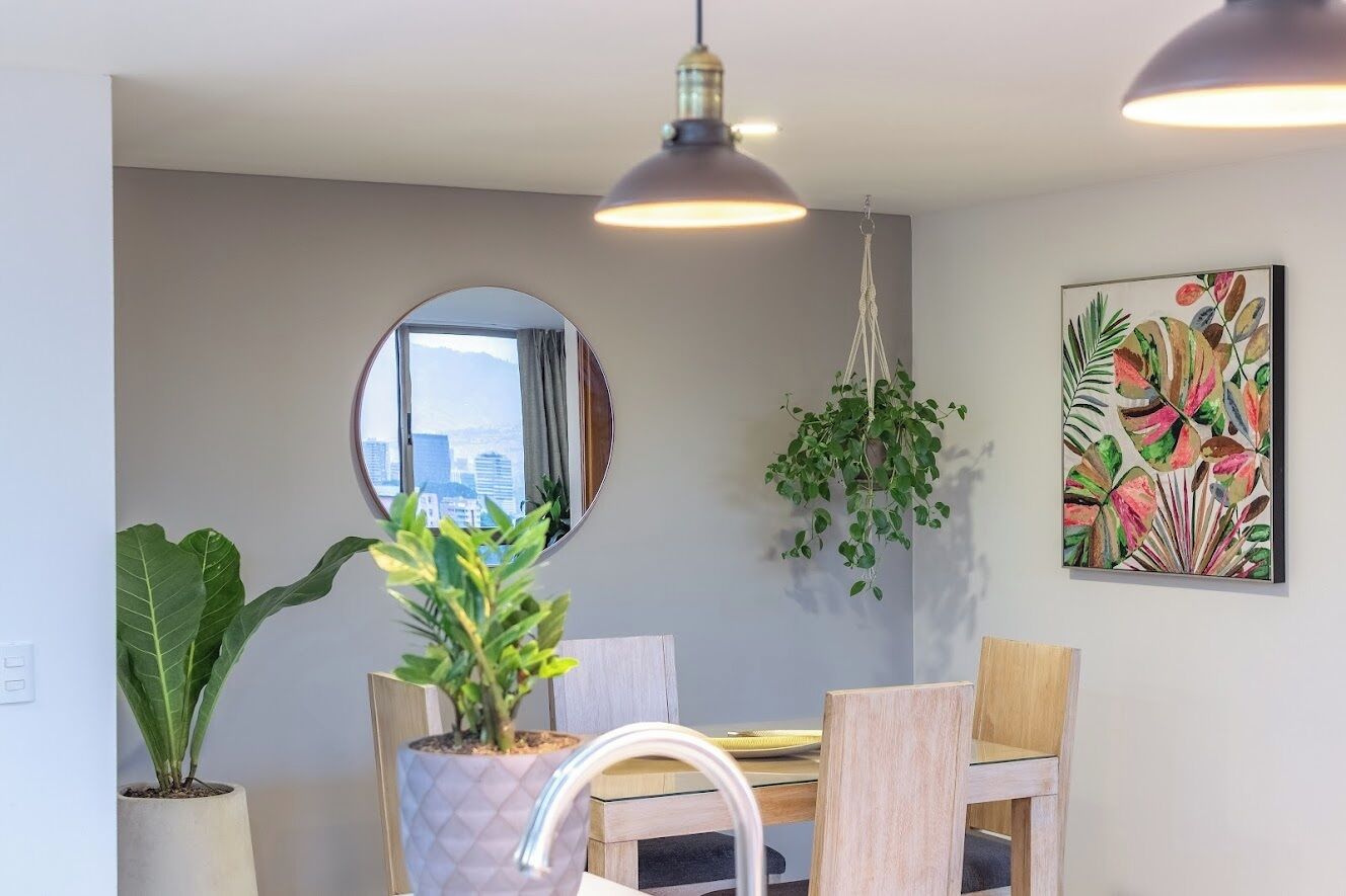 A dining area with a round mirror, hanging plants, and a city view.