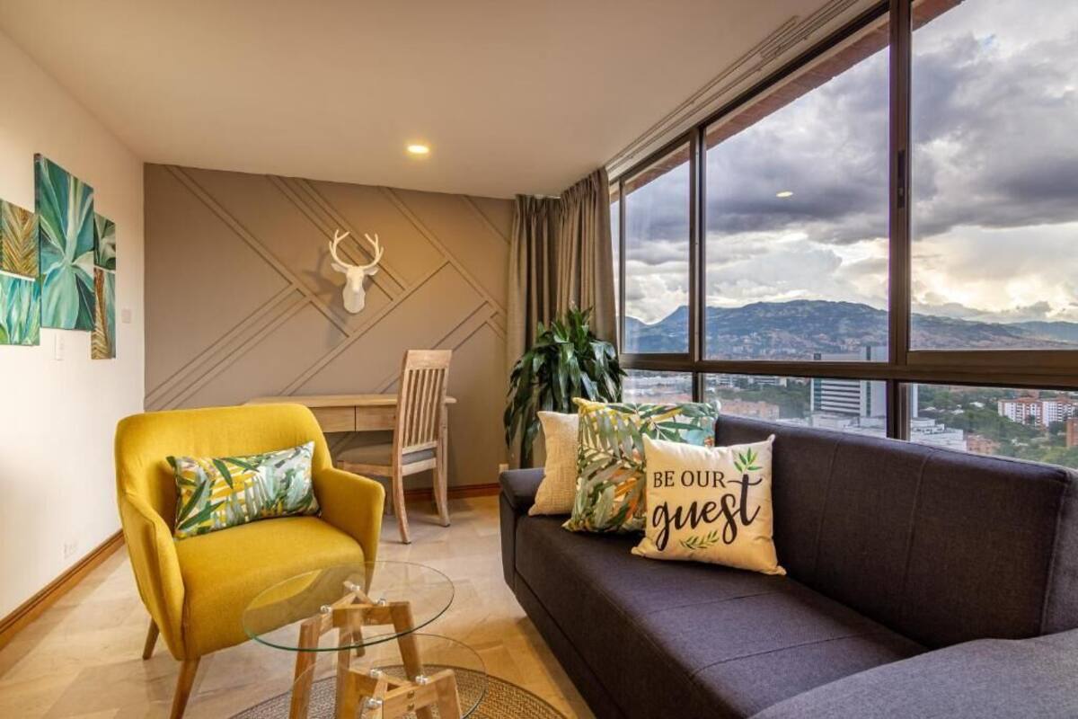 Un salon moderne avec un canapé, un fauteuil et une table à manger. Une grande fenêtre offre une vue sur la ville et les montagnes.