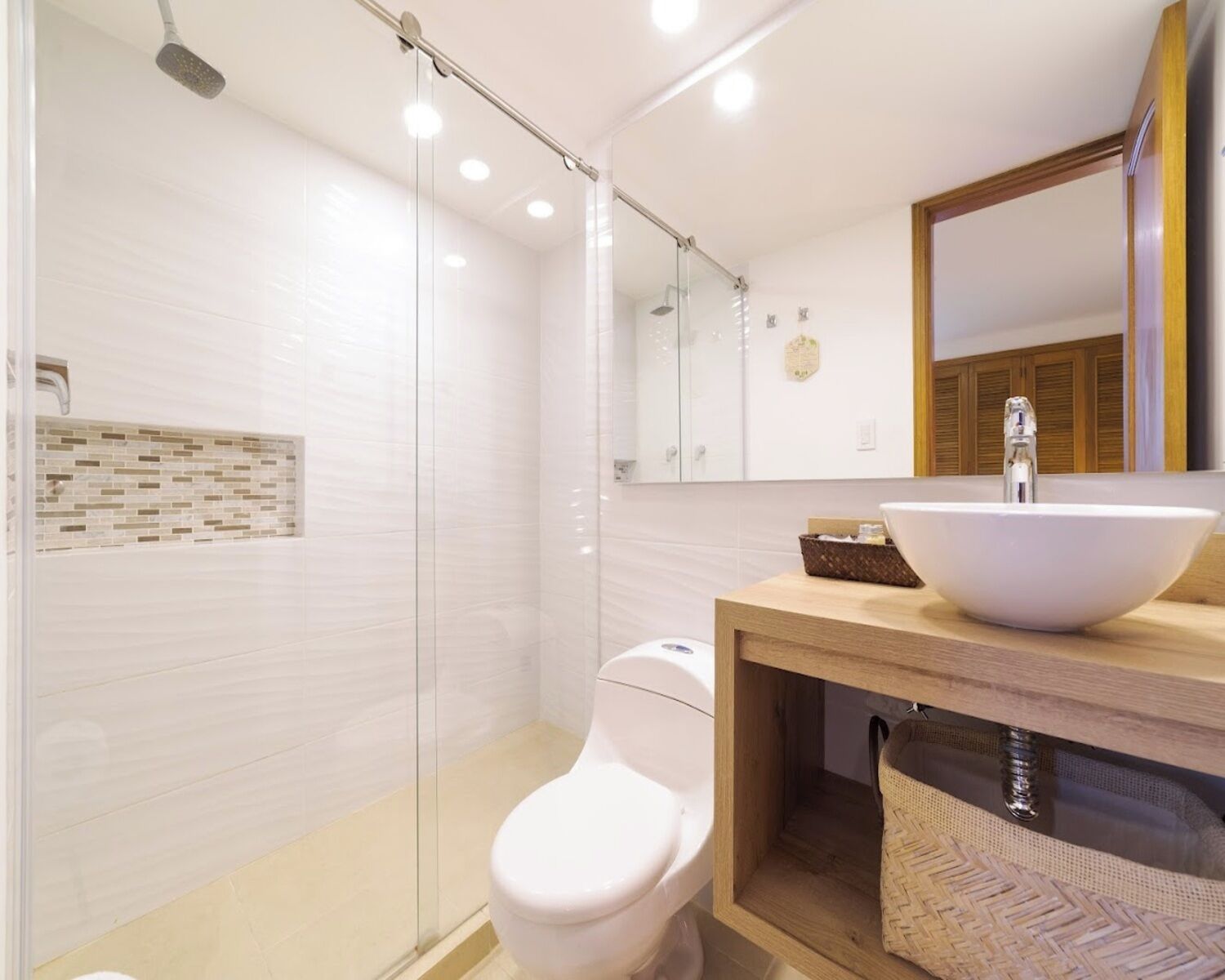 Un baño moderno con cabina de ducha de vidrio, inodoro blanco y tocador de madera con un lavamanos grande y blanco.