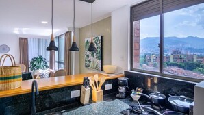 Una cocina moderna con encimeras de granito, luces colgantes y vistas a un paisaje urbano a través de amplios ventanales.