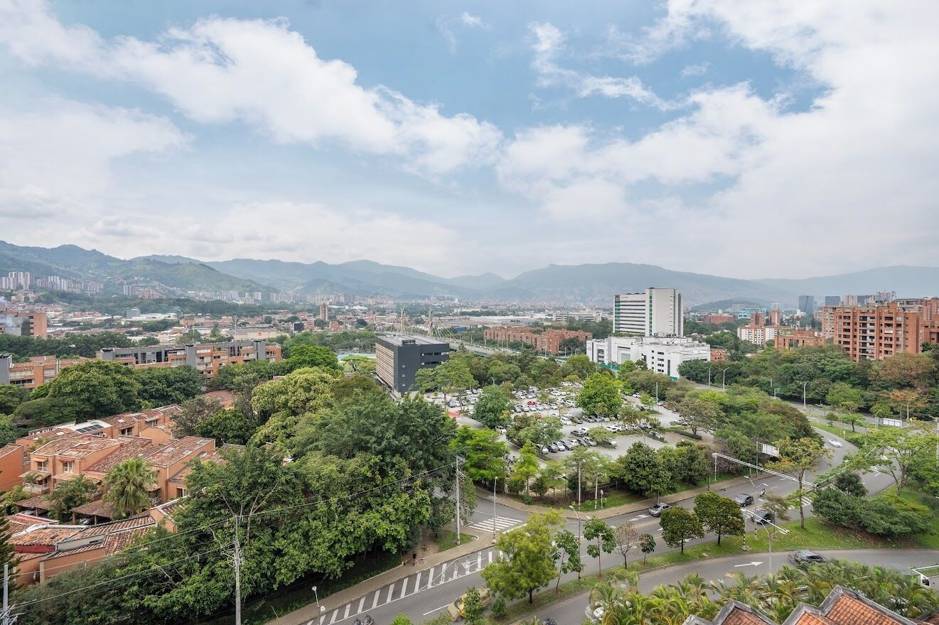 Un paisaje urbano con una combinación de edificios residenciales y comerciales, un moderno rascacielos destacado y zonas verdes circundantes.