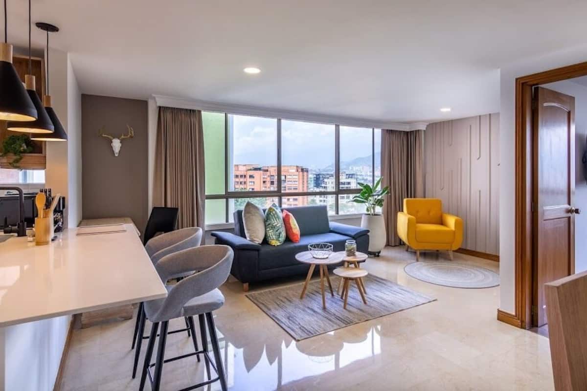 Un salon moderne avec un canapé, un fauteuil jaune et un coin repas doté d’un bar.