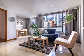 Un salon moderne avec une table basse en verre, un canapé, un fauteuil et une grande fenêtre avec des rideaux.