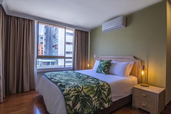 Une chambre d’hôtel avec un grand lit, une table de chevet, une lampe et une fenêtre avec des rideaux.