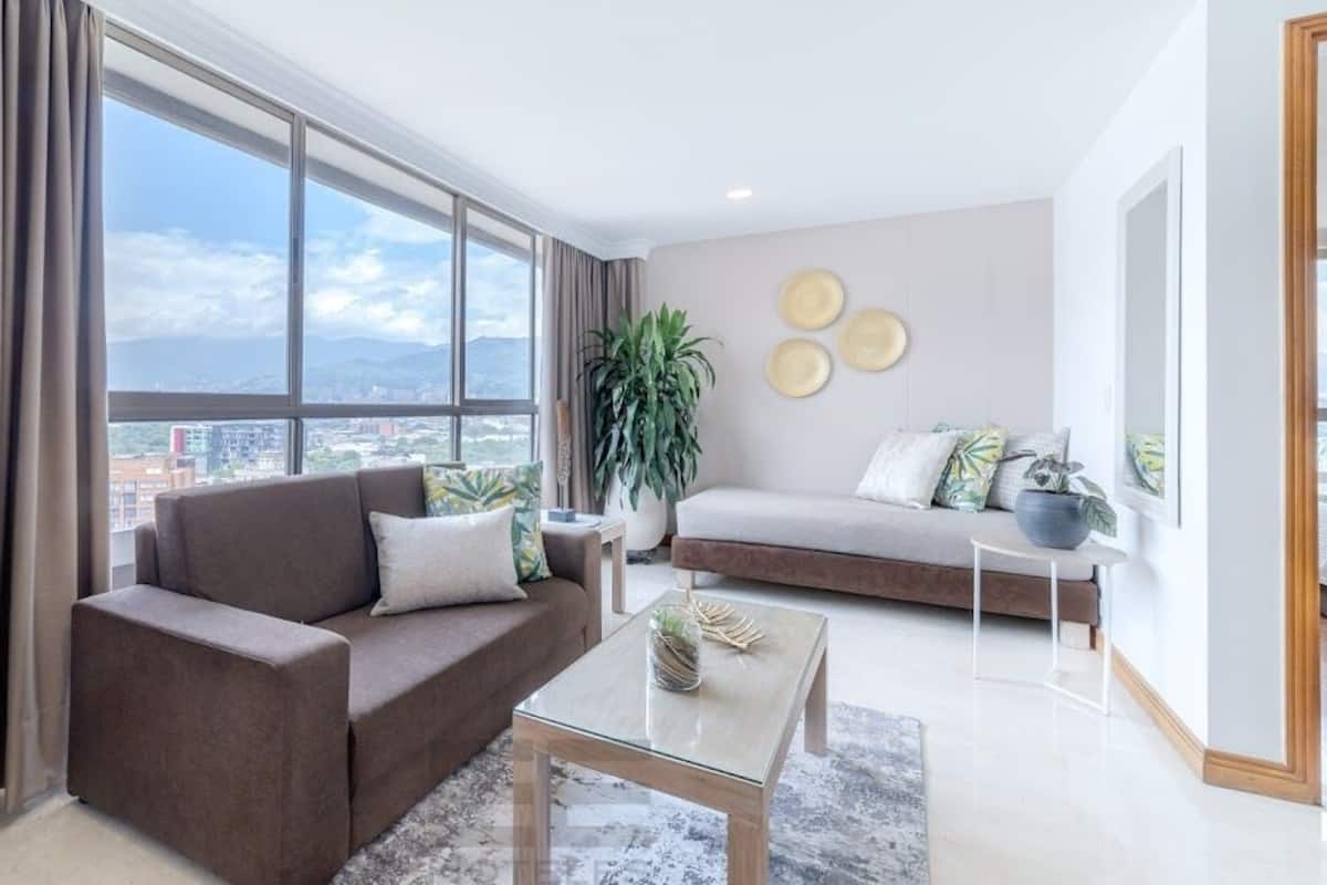 Un salon moderne avec un canapé, une table basse et une grande fenêtre donnant sur la ville.