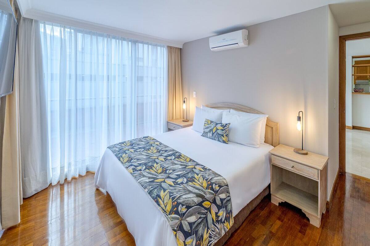 Une chambre d’hôtel avec un grand lit, une table de chevet, un appareil de climatisation et une fenêtre avec des rideaux.