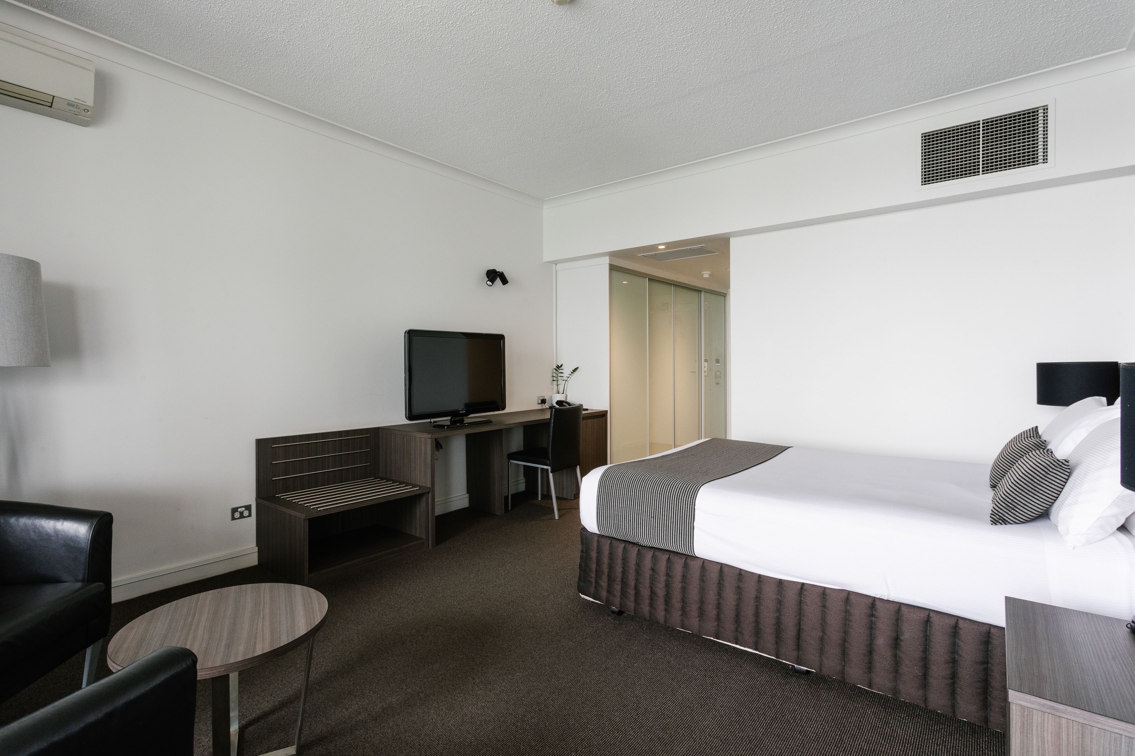 Ein Hotelzimmer mit Bett, Schreibtisch mit Computer, Fernseher, Stuhl und einem kleinen Tisch.