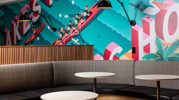 Un área de descanso moderna con un mural colorido, una pared de listones de madera y un espacio con mesas redondas.