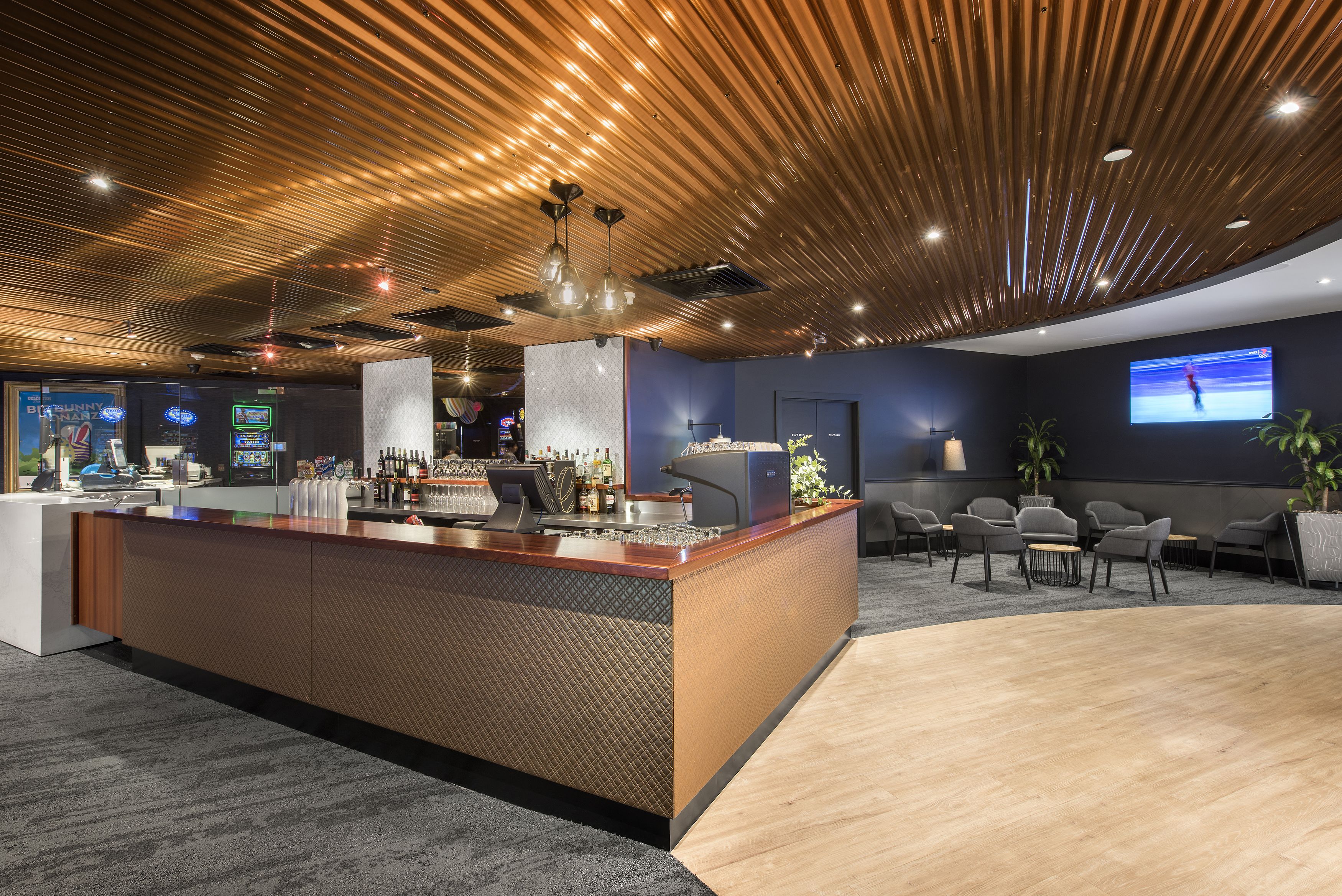 A modern reception area with a wooden reception desk, a large flat-screen TV, and a seating area with chairs and a coffee table.