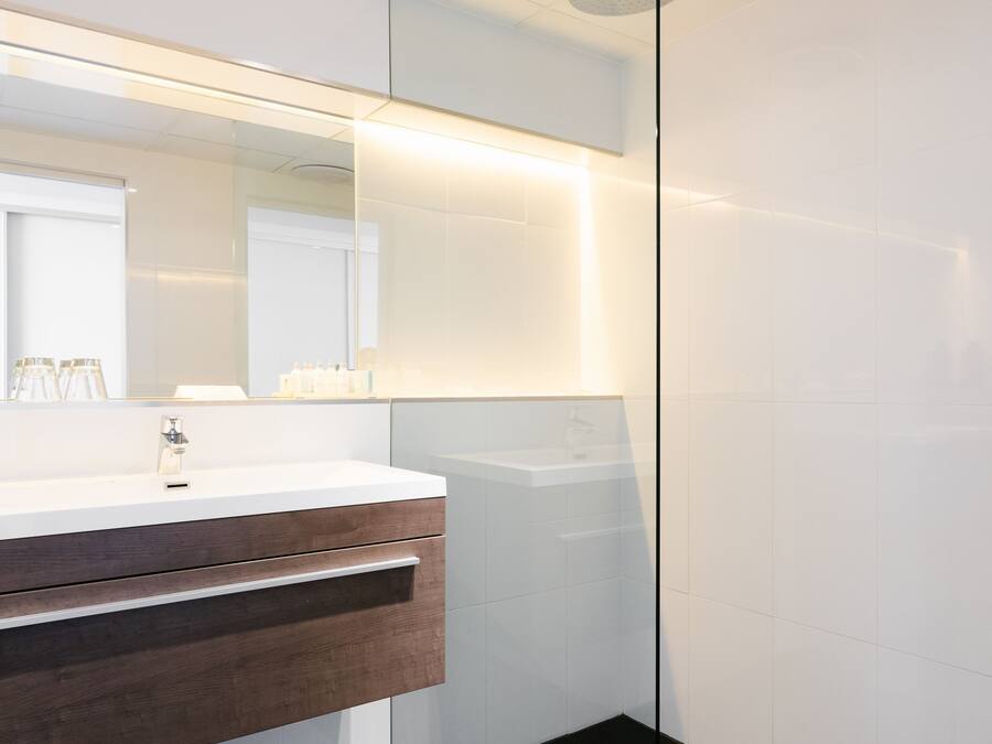 A modern bathroom with a white vanity, dark floor tiles, and a glass shower enclosure.
