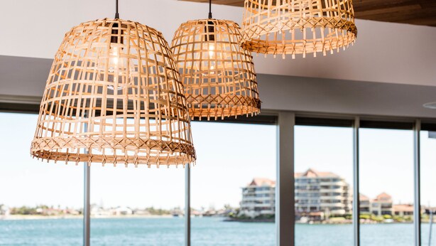 Three woven pendant lights hanging from a ceiling with a view of a body of water and buildings in the background. - Lakes Hotel (West Lakes)