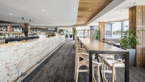 A modern bar area with a marble counter, wooden chairs, and potted plants. - Lakes Hotel (West Lakes)