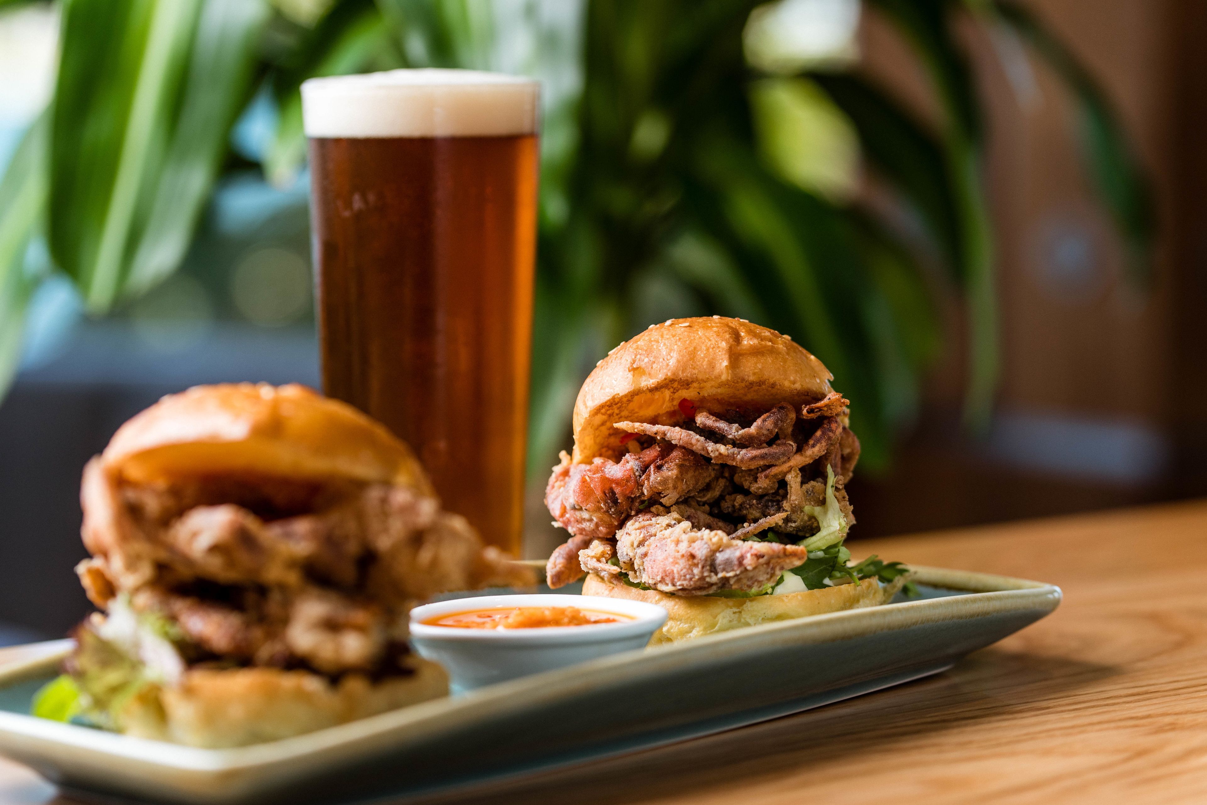 A sandwich with a side of sauce and a glass of beer on a plate.