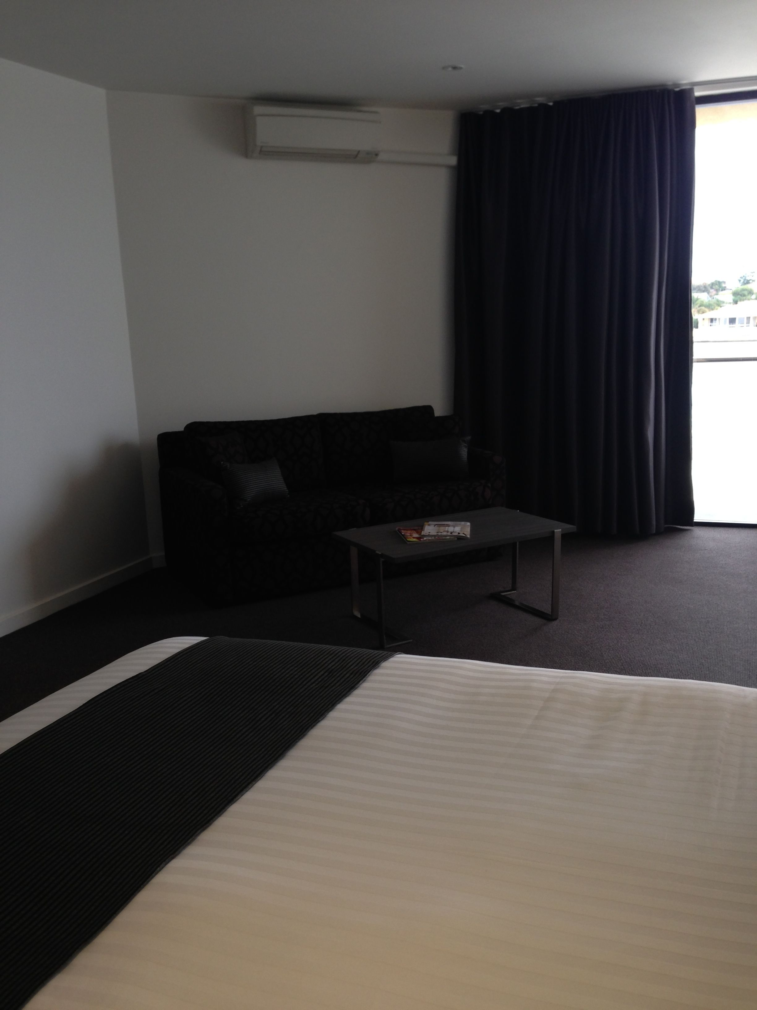 A hotel room with a bed, a small table, a sofa, and a window with curtains.