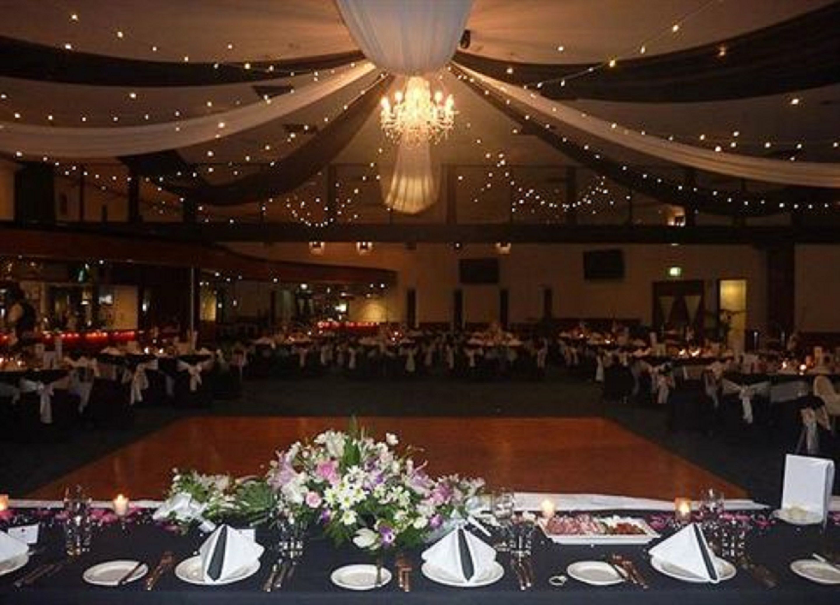 Une salle de banquet où les tables sont dressées pour un événement formel, avec un lustre et des étoffes décoratives suspendues au plafond.