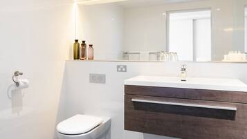 Un baño moderno con inodoro blanco, tocador con espejo y piso de baldosas oscuras.