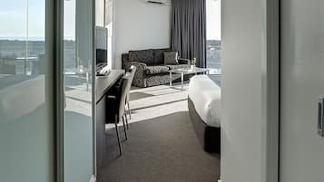 Una habitación de hotel moderna con una cama grande, un escritorio, una silla, un sofá y vistas a la ciudad.