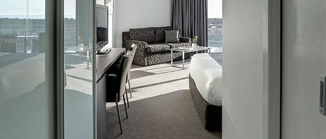 Una habitación de hotel moderna con una cama grande, un escritorio, una silla, un sofá y vistas a la ciudad.