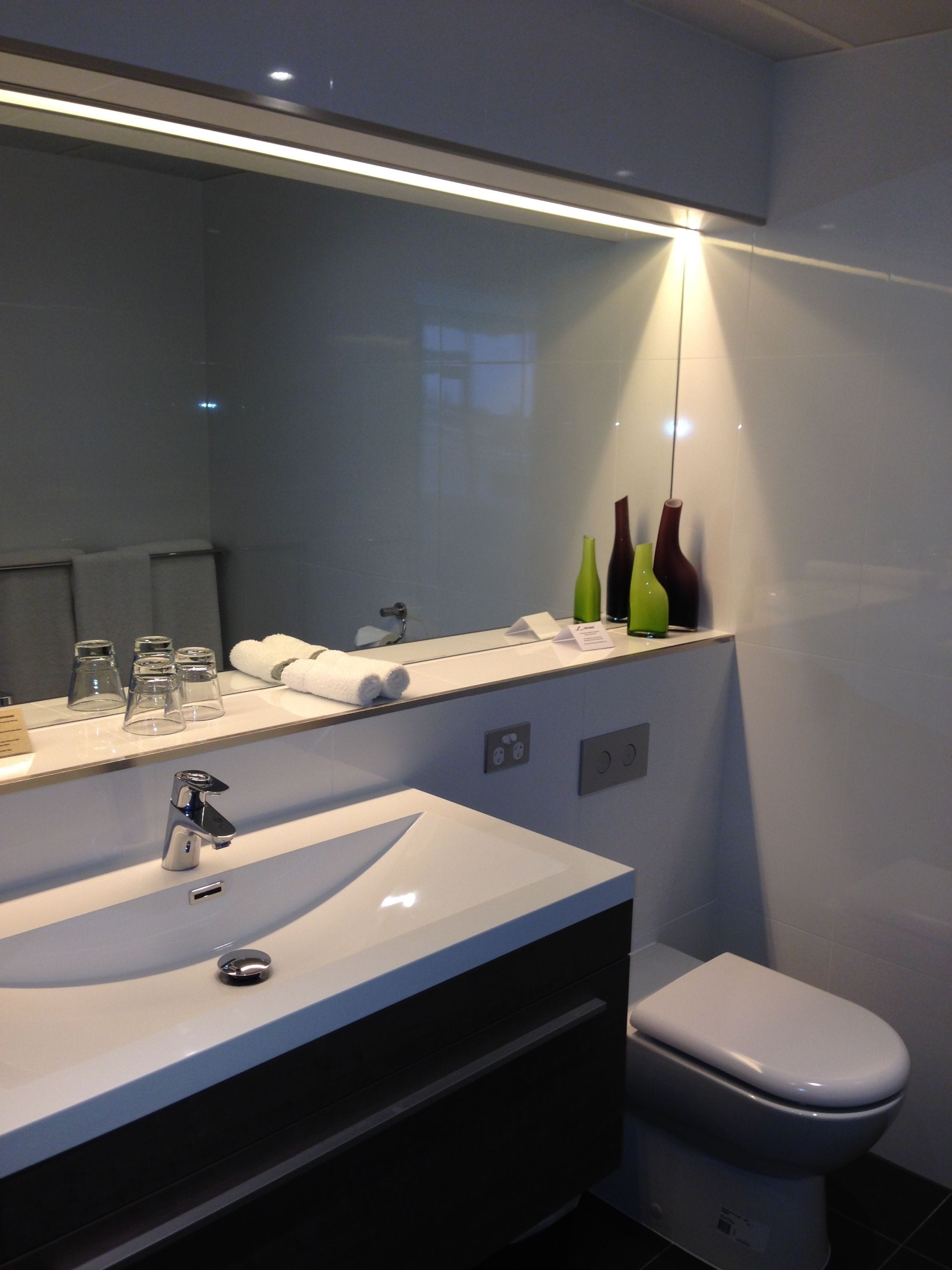 A modern bathroom with a large mirror, a white sink, and a toilet.