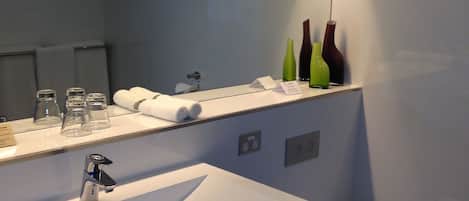 A modern bathroom with a large mirror, a white sink, and a toilet.