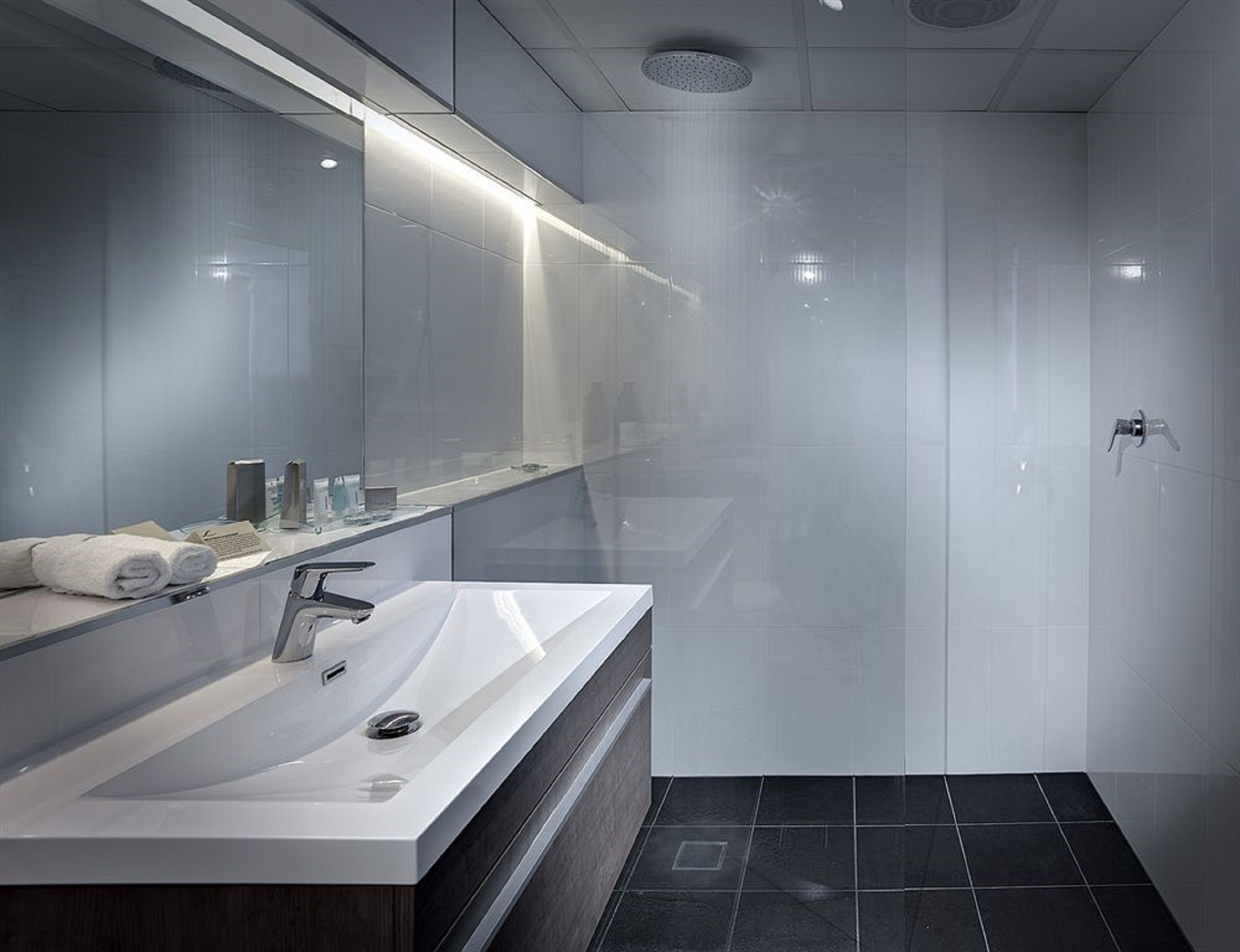 A modern bathroom with a large mirror, a sink, and a shower area.