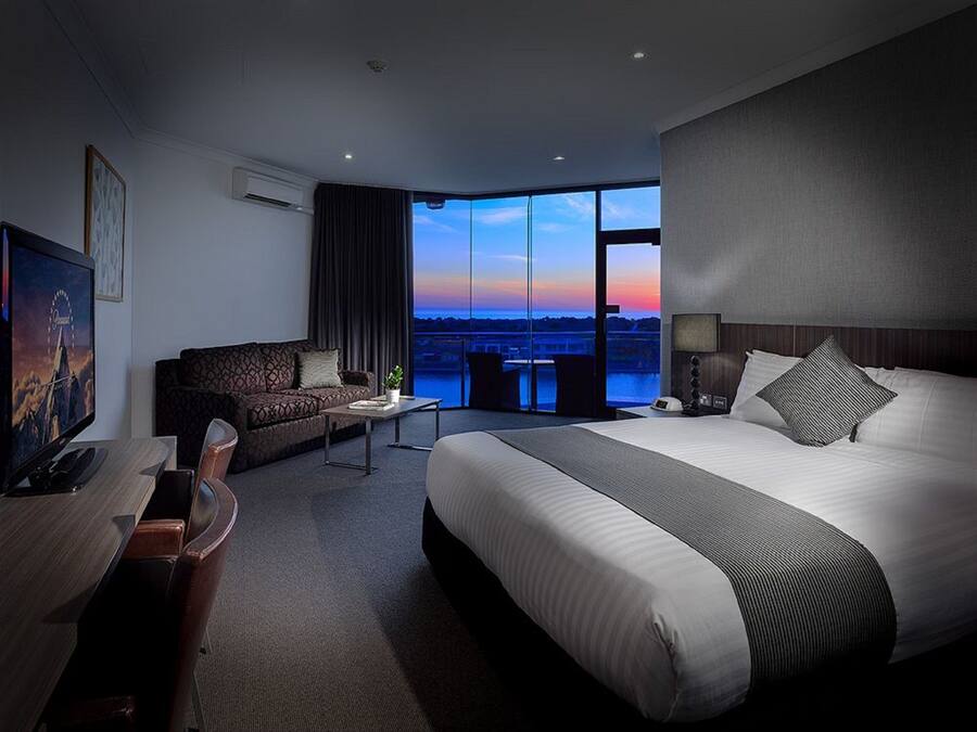 Quarto de hotel moderno com uma cama grande, um sofá, uma escrivaninha e uma televisão.