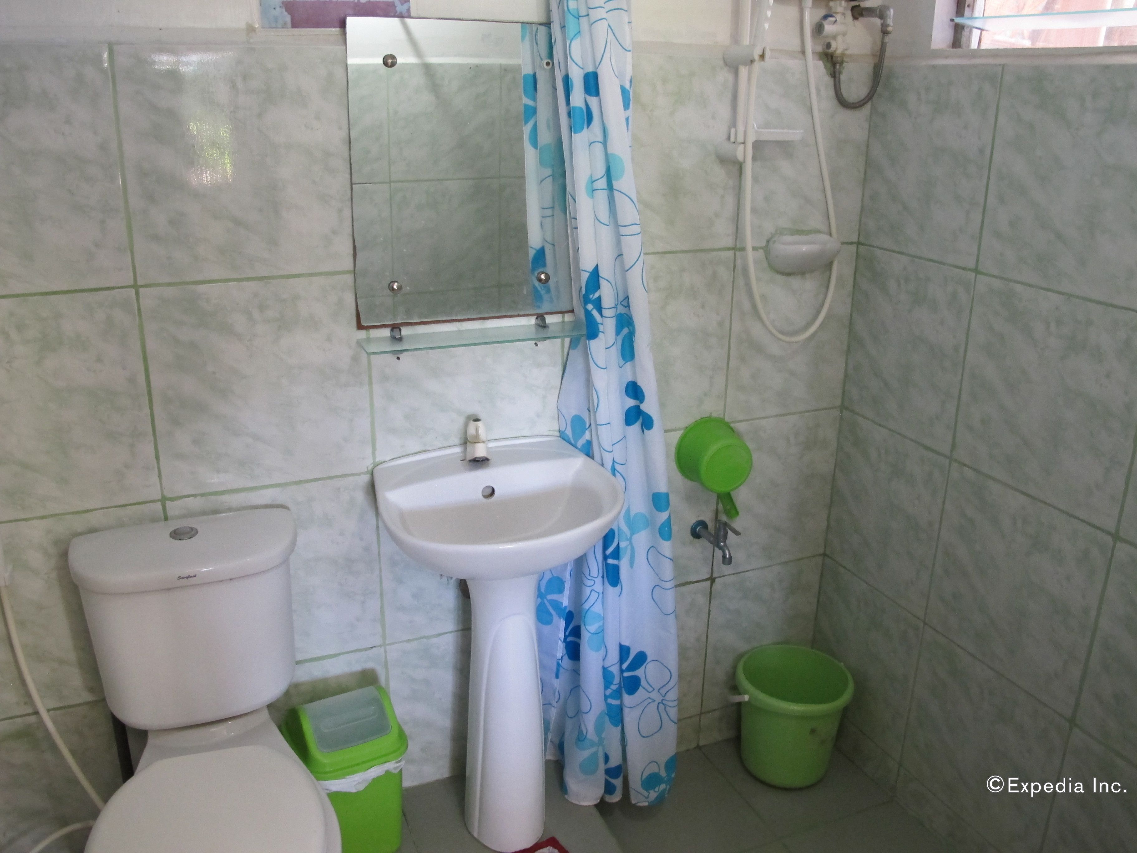 A bathroom with a toilet, sink, shower, and green trash bin.