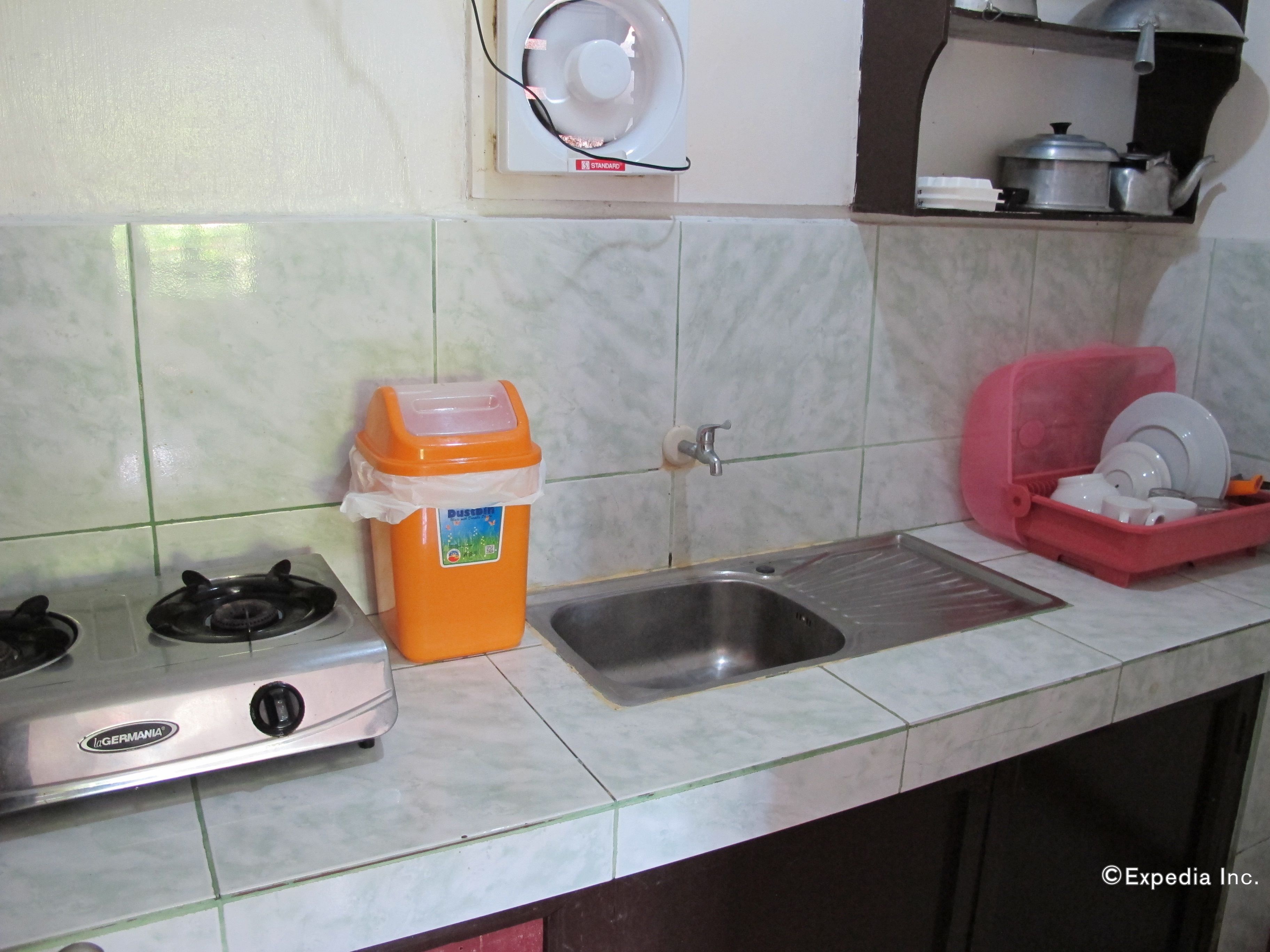 Una cocina con estufa a gas, un lavamanos y un cubo de basura.
