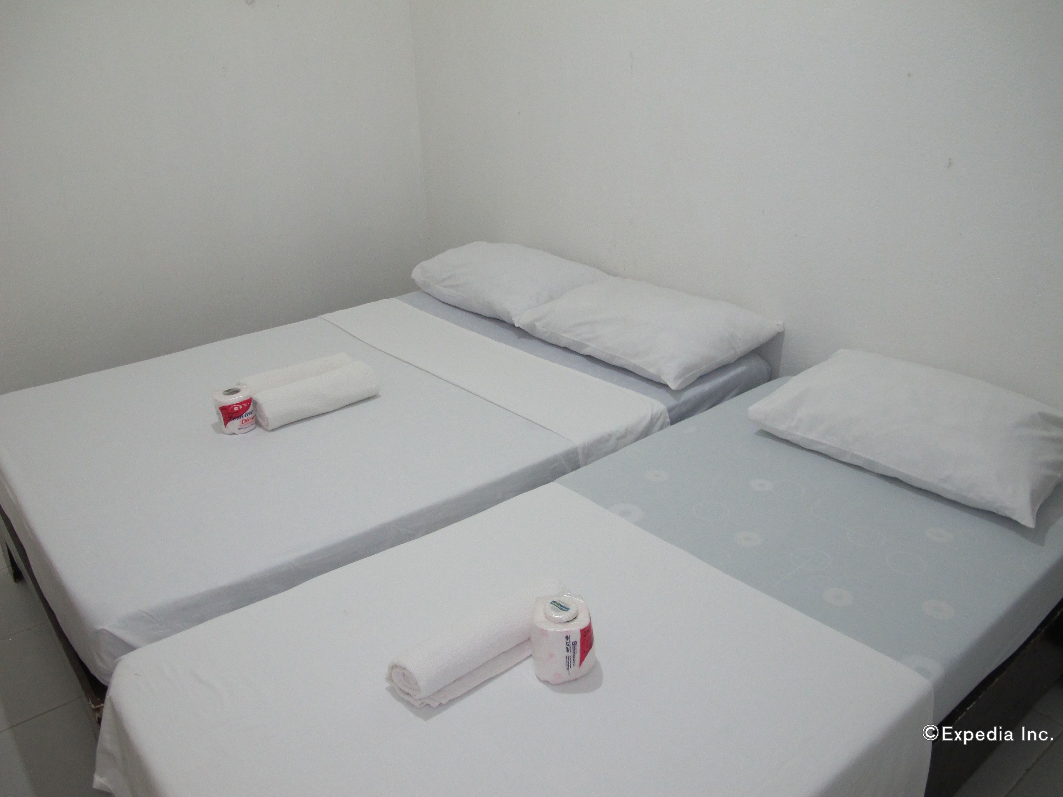 A small, clean room with two single beds, each with a pillow and a rolled towel.
